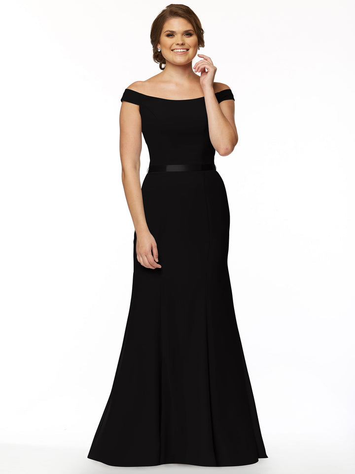A woman models Avery Austin’s 80079, an off-the-shoulder, floor-length black chiffon bridesmaid dress, standing against a white background with a gentle smile and her hand at her waist.
