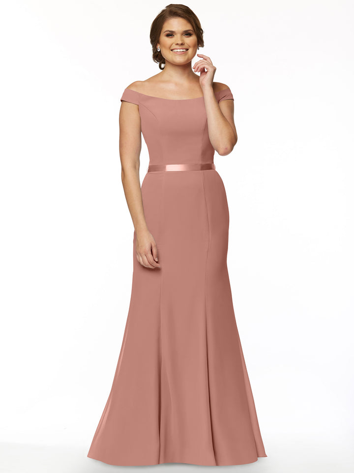 A woman smiles in Avery Austin’s floor-length, off-the-shoulder 80079 bridesmaid dress, featuring a satin waistband and fit-and-flare silhouette, her hair styled neatly against a plain white background.