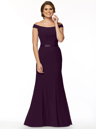 A woman poses against a white background in Avery Austin’s 80079, an elegant off-the-shoulder bridesmaid dress. The floor-length dark purple gown features a fitted bodice and flared skirt, flattering her figure as she smiles with neatly styled hair.