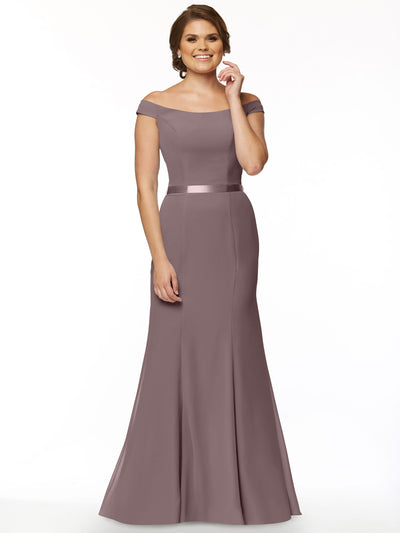 A woman with short brown hair smiles slightly while wearing Avery Austin’s 80079: an elegant mauve off-the-shoulder bridesmaid dress featuring a satin waistband and flared skirt, set against a white background.
