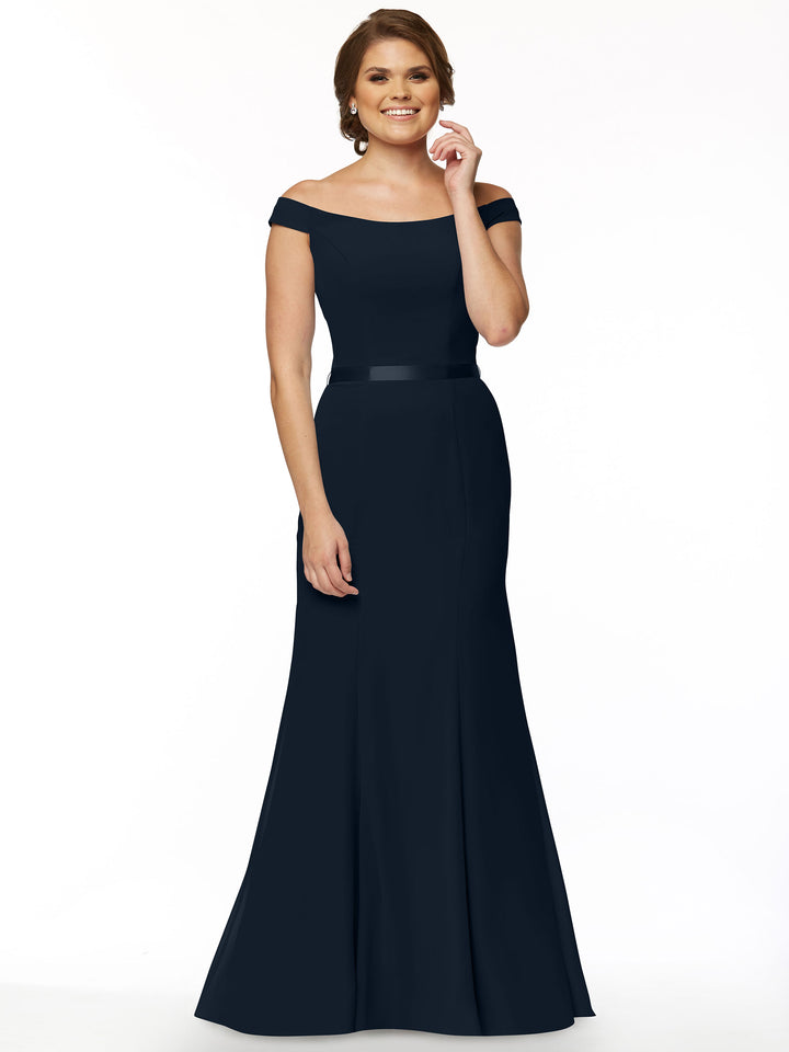 A woman smiles in the Avery Austin 80079, an off-the-shoulder, floor-length navy bridesmaid dress with a fitted bodice and flared skirt, set against a plain white background.