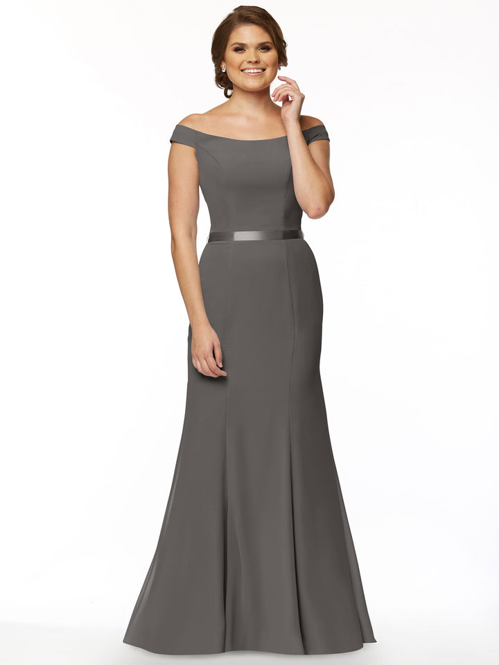 A woman models Avery Austin’s 80079: an off-the-shoulder, floor-length gray chiffon bridesmaid dress with a satin waistband. She smiles in an updo against a plain white background.
