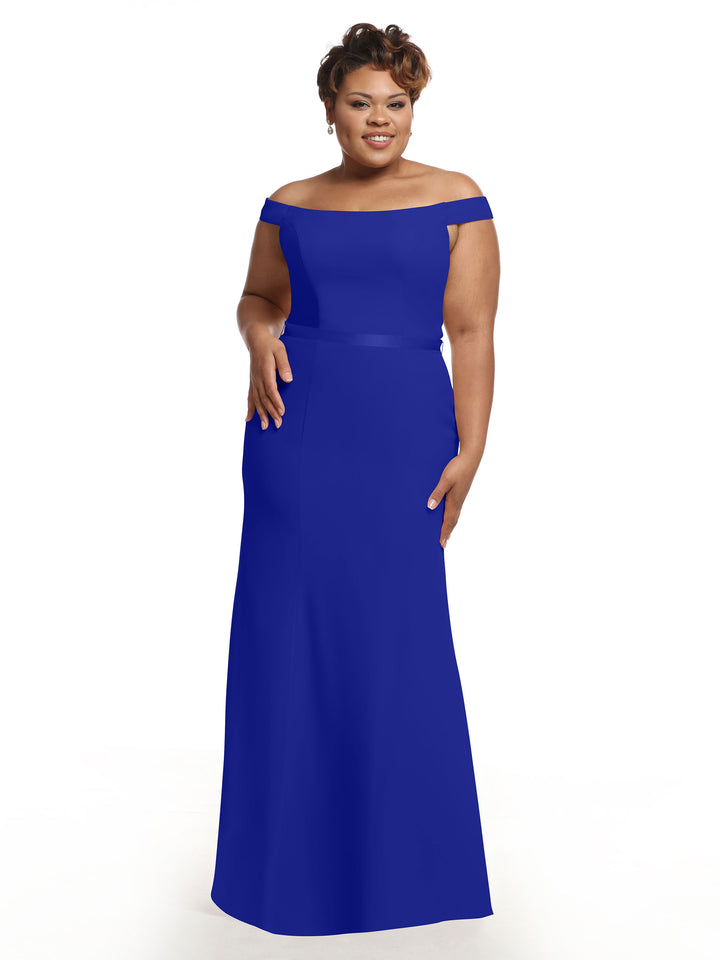 A woman models Avery Austin style 80079, an off-the-shoulder bridesmaid dress in Cobalt, standing against a plain white background with a smile, one hand at her side and the other by her hip.