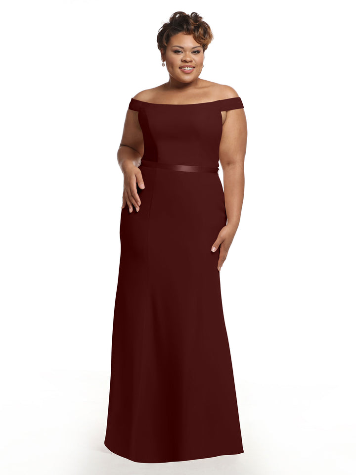 A woman smiles against a white background wearing Avery Austin style 80079, a merlot off-the-shoulder bridesmaid dress in chiffon with an elegant fit-and-flare silhouette, one hand at her side and the other touching her hip.