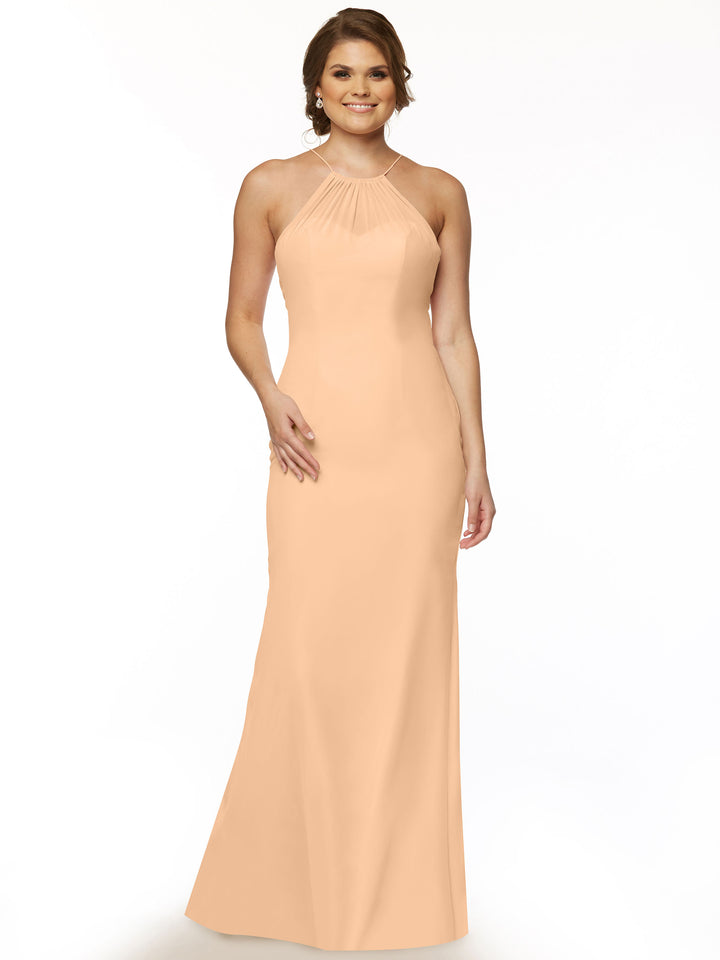A woman smiles in the Avery Austin 80083, a blush chiffon halter dress with a keyhole back. The sleeveless, floor-length gown flatters her figure. She wears earrings and a ring, her wavy hair styled back. The background is white.