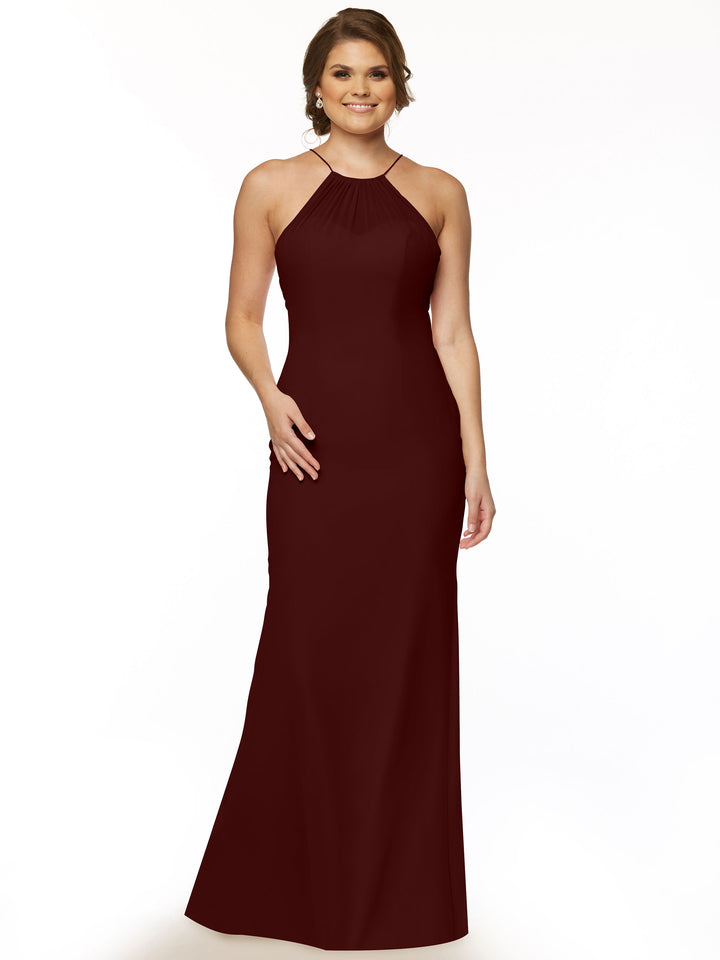 A woman in the Avery Austin 80083, a sleeveless floor-length merlot dress with a high halter neckline and keyhole back, stands smiling against a white background with one hand on her hip.