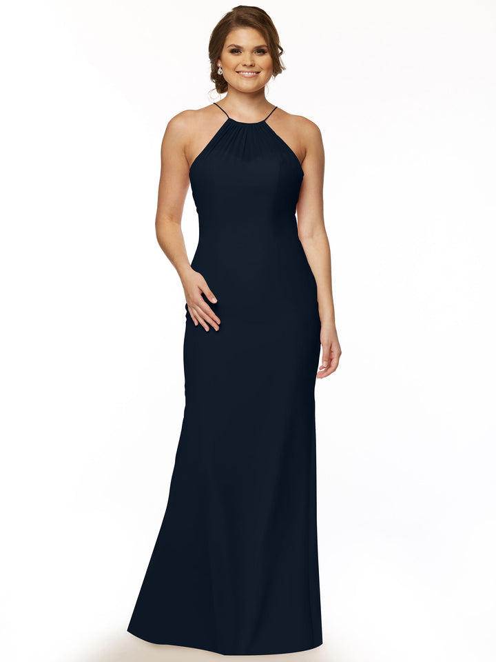 A woman stands smiling with one hand on her hip, wearing Avery Austin style 80083, a sleeveless, floor-length dark navy chiffon halter dress, against a plain white background.