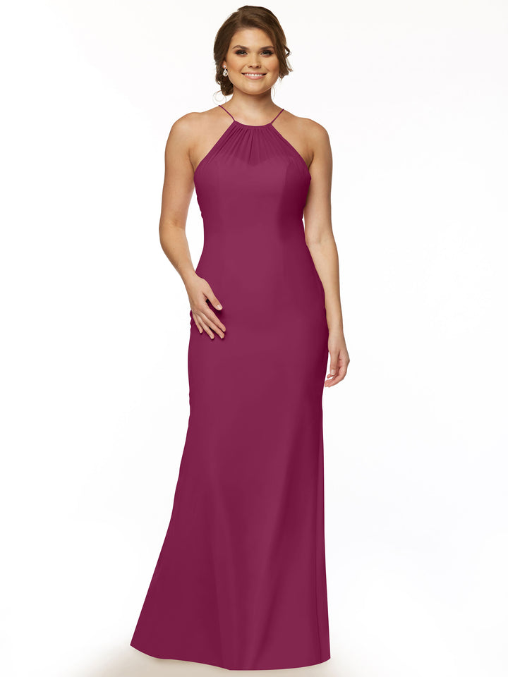 A woman stands smiling against a plain white background, wearing Avery Austin’s magenta chiffon halter dress (style 80083) featuring a floor-length silhouette, sleeveless design, and keyhole back.