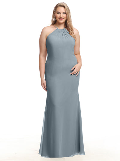 A woman models Avery Austin's 80083 dress—a floor-length slate blue halter gown featuring a keyhole back and fitted sleeveless chiffon silhouette—smiling with her long wavy blonde hair draped over one shoulder.