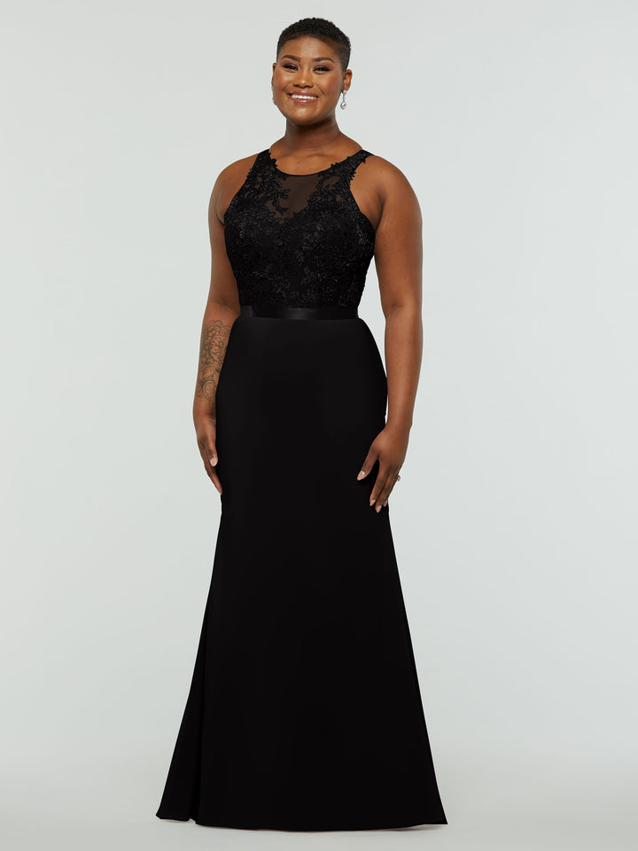 A woman smiles in Avery Austin’s 80095: a sleeveless, floor-length black gown with lace bodice, satin waistband, and fit-and-flare silhouette, posed against a plain light gray background.