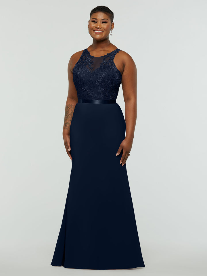 A smiling person poses against a light gray background in Avery Austin’s 80095 bridesmaid dress in Midnight, featuring a chiffon fit-and-flare silhouette with a lace bodice and satin waistband.