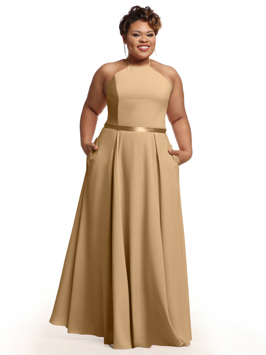 A woman models Avery Austin’s 80099 dress: a sleeveless, floor-length tan satin A-line with a halter neckline and pockets, smiling against a white background.
