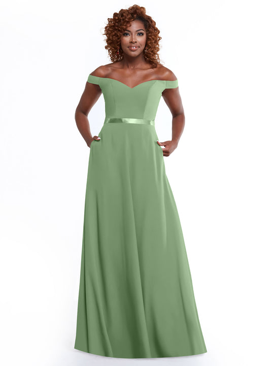A woman with curly hair models the Avery Austin 80100, a sage green off-the-shoulder dress with a fitted bodice, satin waistband, and A-line skirt, standing against a plain white background.