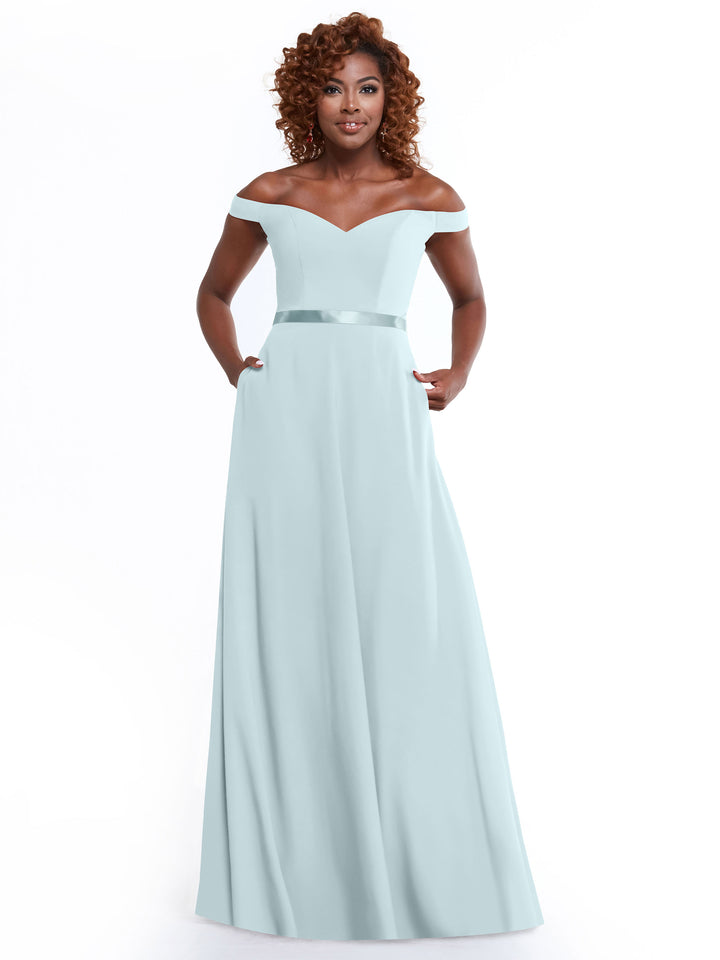 A woman with curly hair wears the Avery Austin TH-80100, a sky blue off-the-shoulder A-Line dress with a fitted bodice, waistband detail, and pockets, standing against a plain white background.