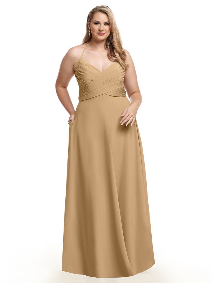A woman wears the Avery Austin 80101—a long, gold-beige A-line dress with spaghetti straps and a fitted bodice—posing against a white background with one hand in her pocket.