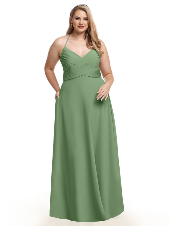 A woman models Avery Austin's 80101, a sleeveless sage green A-line dress with a V-neckline and ruched bodice, standing against a white background with one hand in her pocket.