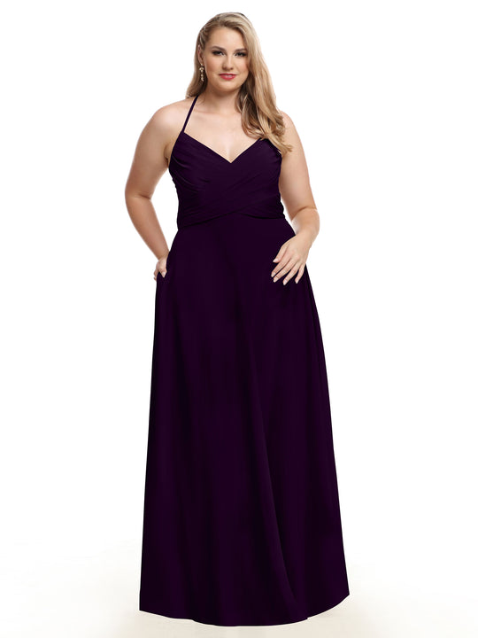 A woman in Avery Austin’s TH-80101 floor-length A-line dress, featuring an eggplant hue with a pleated bodice and flowing skirt, stands against a plain white background.