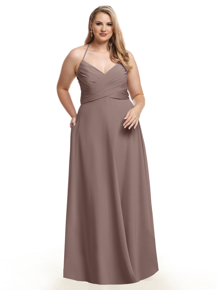 A woman with long wavy blonde hair poses with one hand in her pocket, wearing Avery Austin 80101—a mauve A-line dress featuring a pleated bodice, V-neckline, and flowing skirt—against a white background.