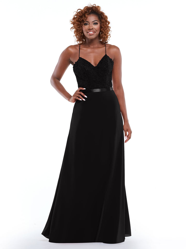 A woman with curly hair smiles in front of a white background, wearing Avery Austin 80103—a sleeveless black gown with a spaghetti strap lace bodice, fitted sequin top, and a long slit A-line skirt.