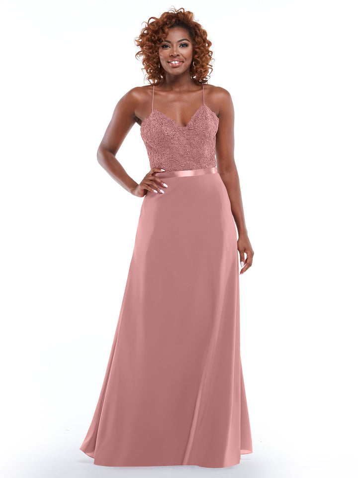 A woman with curly hair models Avery Austin’s 80103 gown in dusty rose—a sleeveless, floor-length dress with spaghetti strap lace bodice, V-neckline, and a flowing A-line skirt with a slit—standing against a white background.