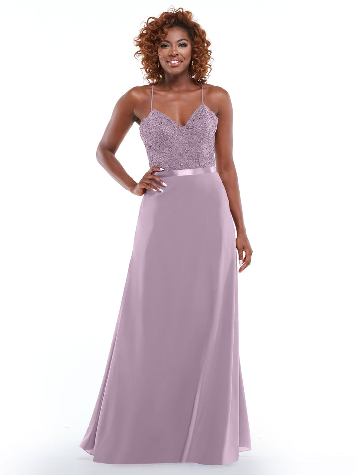 A woman wearing Avery Austin’s 80103 lavender floor-length dress with spaghetti strap lace bodice, satin waistband, and slit A-line skirt stands smiling against a white background.