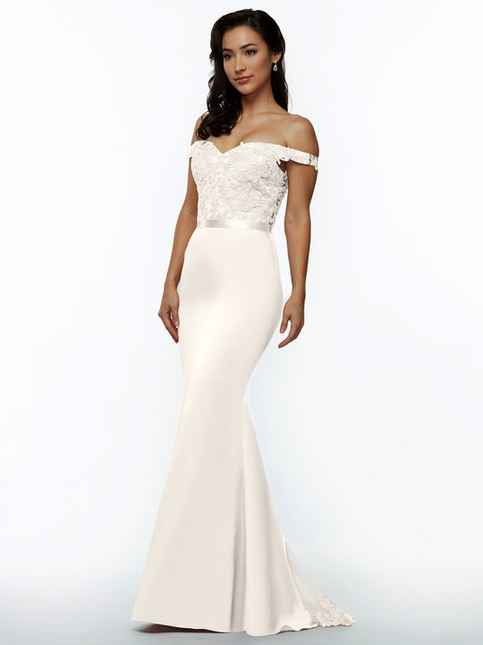 A woman models Avery Austin’s 80104, an off-the-shoulder, form-fitting white wedding dress with lace bodice detailing and a smooth, floor-length skirt, set against a simple light background.