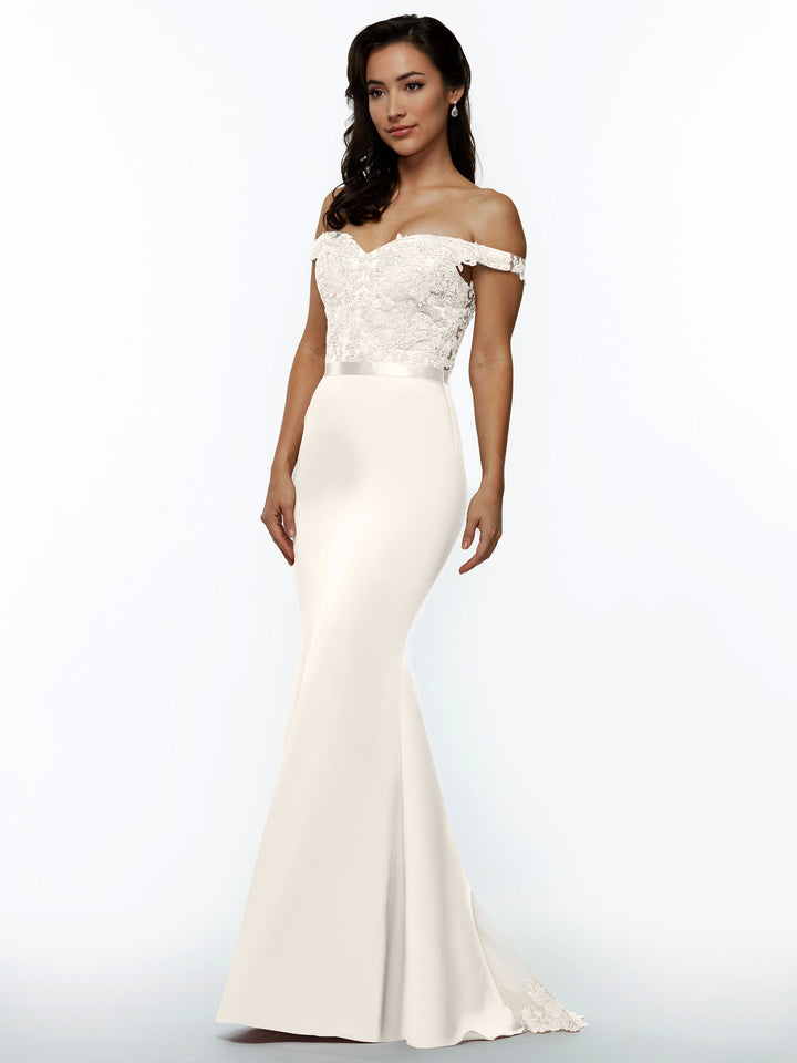 A woman models Avery Austin’s 80104, an off-the-shoulder, form-fitting white wedding dress with lace bodice detailing and a smooth, floor-length skirt, set against a simple light background.