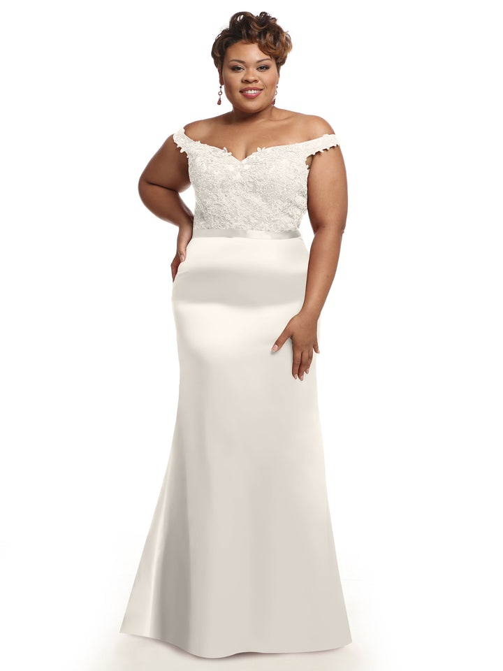 A woman in Avery Austin’s 80104 off-the-shoulder bridesmaid dress with a lace bodice and smooth, floor-length skirt smiles with one hand on her hip against a plain white background.