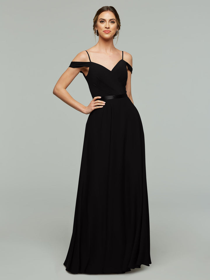 A woman poses with one hand on her hip, wearing the Avery Austin 80106—a long, elegant black off-the-shoulder bridesmaid dress with thin straps and a fitted bodice. Her hair is styled up against a plain background.