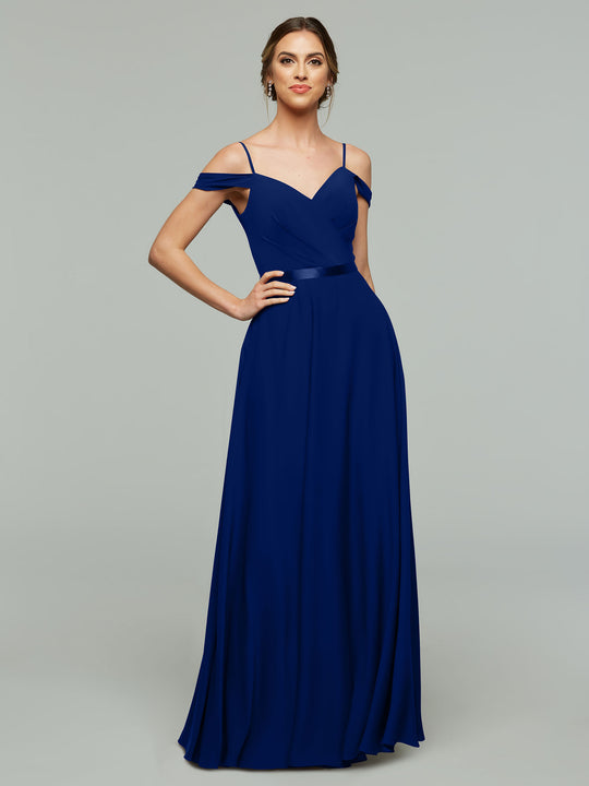 A woman poses confidently in Avery Austin’s 80106: an elegant royal blue chiffon bridesmaid dress with a floor-length A-line skirt, off-the-shoulder thin straps, and a fitted bodice, set against a gray background.