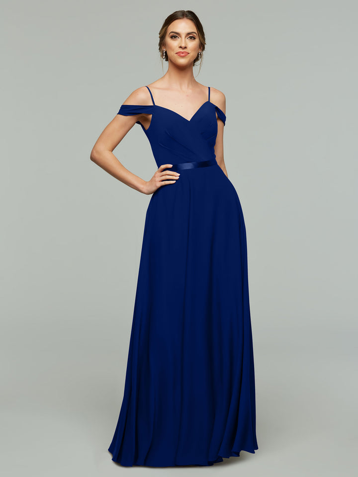 A woman poses confidently in Avery Austin’s 80106: an elegant royal blue chiffon bridesmaid dress with a floor-length A-line skirt, off-the-shoulder thin straps, and a fitted bodice, set against a gray background.