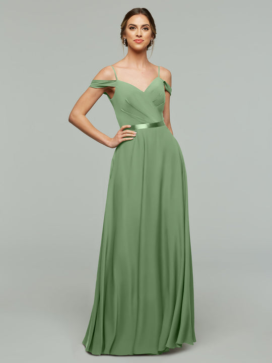 A woman wearing Avery Austin’s 80106, a floor-length sage green A-line dress with a sweetheart neckline and thin straps, stands against a plain light gray background.