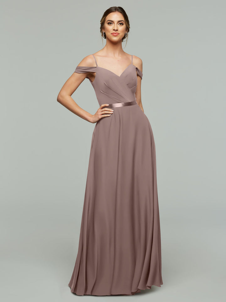 A woman models Avery Austin style 80106—an off-the-shoulder mauve bridesmaid dress with a floor-length A-line silhouette and satin waistband—posing with one hand on her hip against a plain gray background.