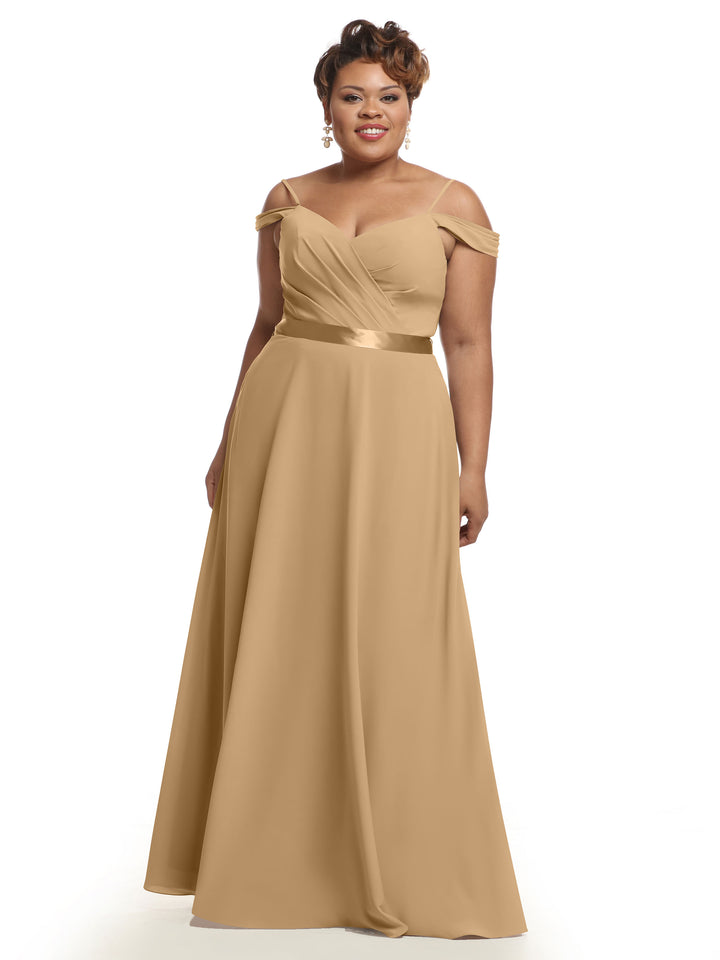 A woman smiles in Avery Austin’s 80106 gold off-the-shoulder bridesmaid dress, featuring a satin waistband and floor-length A-line skirt, against a plain white backdrop.