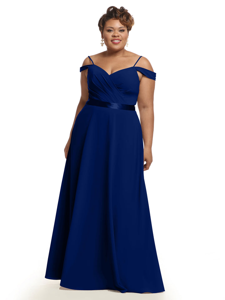 A woman smiles against a plain white background, wearing the Avery Austin 80106 bridesmaid dress in royal blue, featuring a floor-length off-the-shoulder style, V-neckline, and ruched bodice.