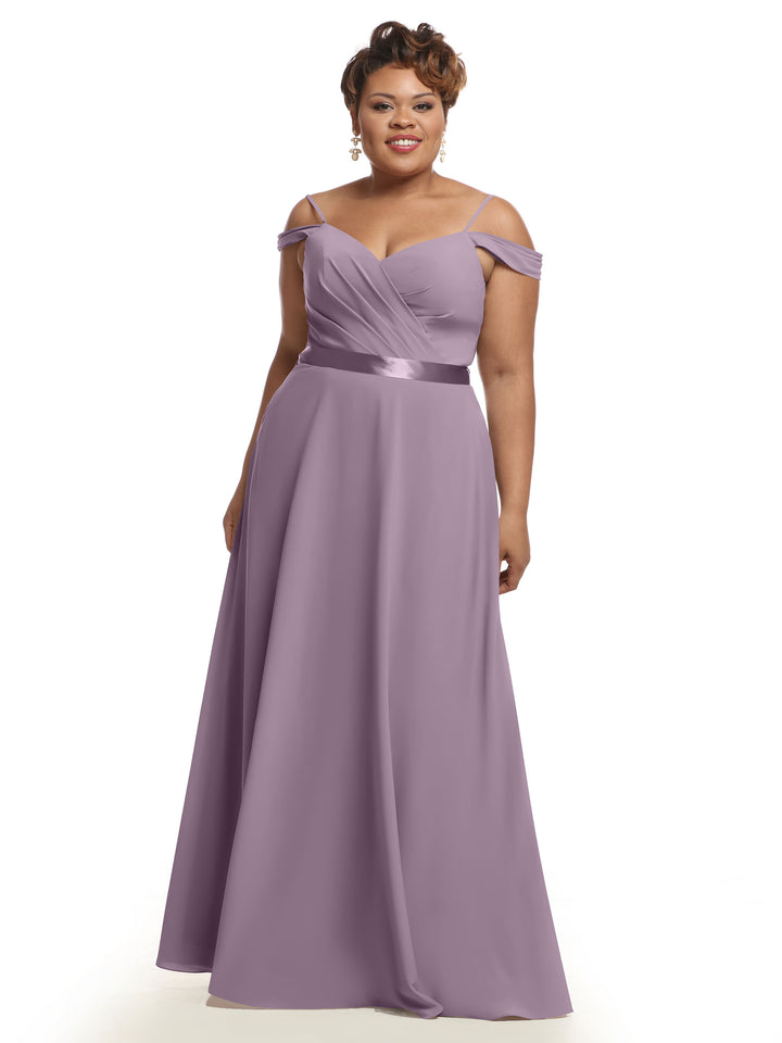 A woman wears the Avery Austin TH-80106, a floor-length, dusty lavender off-the-shoulder chiffon bridesmaid dress with a ruched fitted bodice and satin waistband, smiling against a plain white background.