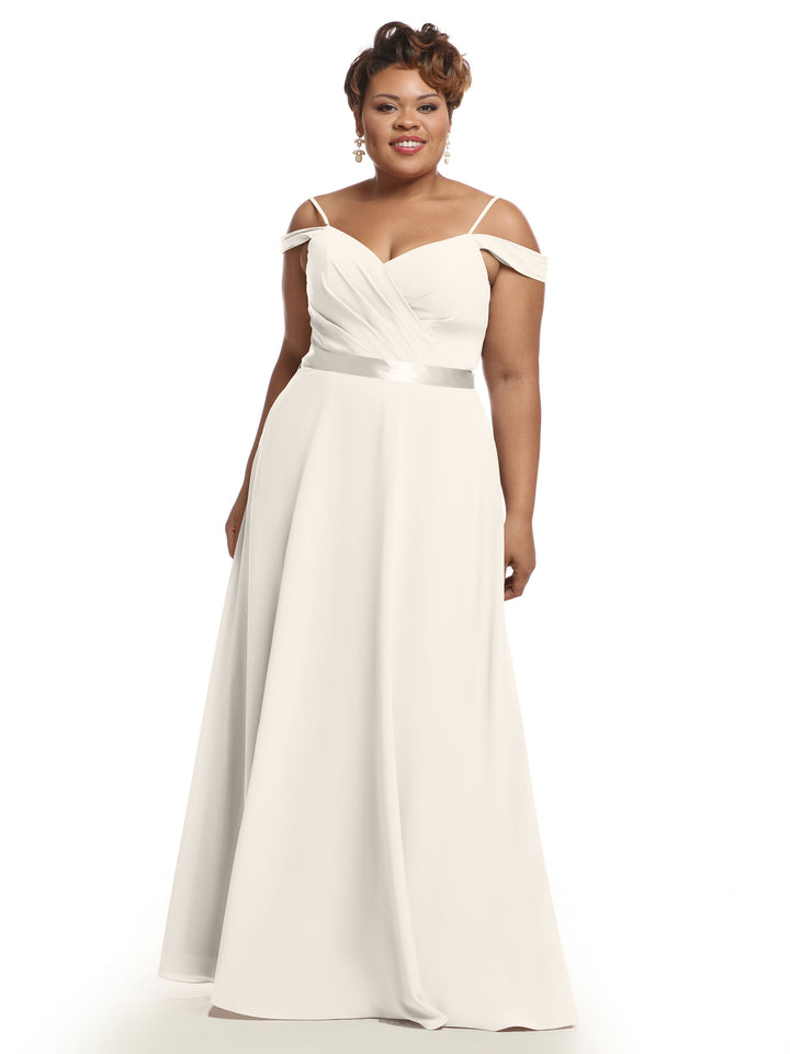 A woman models Avery Austin’s 80106: an ivory, off-the-shoulder A-line bridesmaid dress with a fitted bodice, flowing floor-length skirt, and satin waistband, posing elegantly against a plain white background.