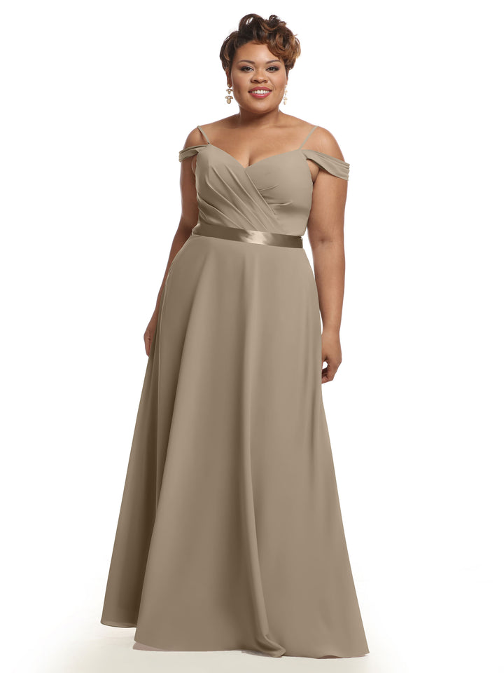 A woman smiles in the Avery Austin 80106 bridesmaid dress, featuring a taupe off-the-shoulder design with a fitted bodice, ruched detailing, satin waistband, and elegant floor-length silhouette against a white background.