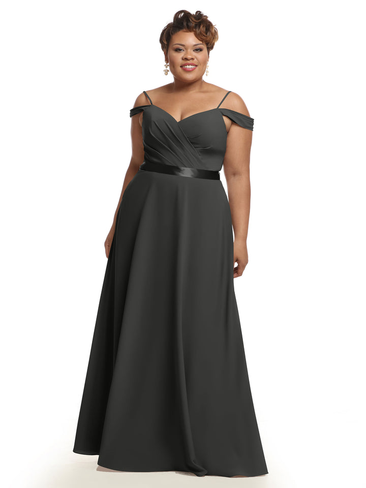 A woman stands smiling against a white background, wearing the Avery Austin 80106—a floor-length, steel gray off-the-shoulder bridesmaid dress featuring a fitted bodice, V-neckline, and flowing skirt.