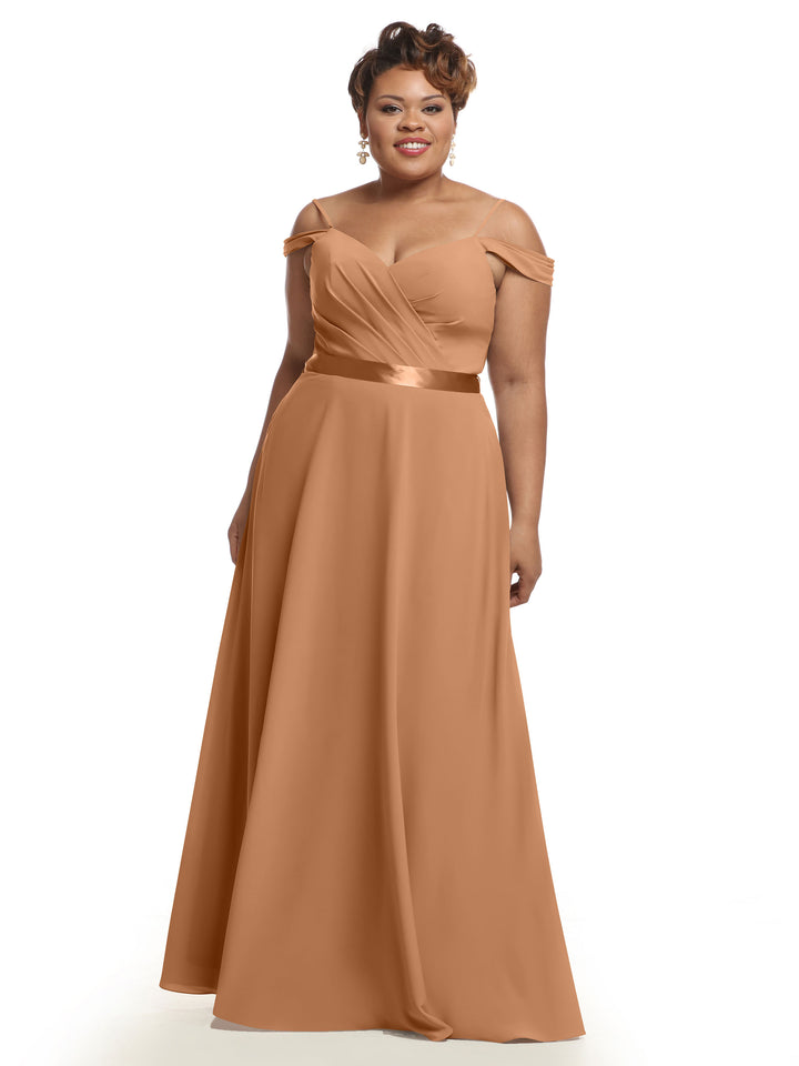 A woman smiles against a white background in Avery Austin’s 80106, a floor-length, off-the-shoulder bridesmaid dress in light brown featuring a fitted bodice, ruched detailing, and a satin waistband.