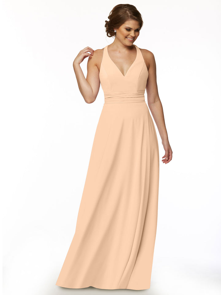 A woman models the Avery Austin 80107 dress—a peach, sleeveless A-line with a deep V-neck—standing against a white background, smiling and looking down with her brown hair in a feminine updo.
