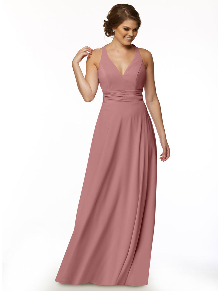 A woman wearing Avery Austin’s 80107, a sleeveless A-Line dress with a deep V-neck and ruched waist, stands against a plain white background, smiling and looking down.