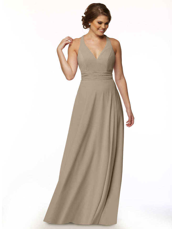 A woman wearing the Avery Austin 80107—a feminine, sleeveless taupe A-line dress with a V-neckline and fitted waistband—stands against a white background, looking down and smiling with one hand near her hair.