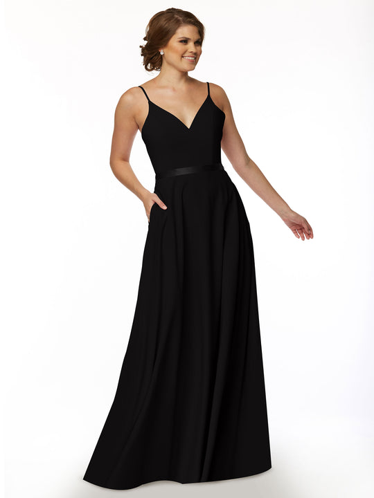 A woman smiles against a plain white background wearing Avery Austin's 80112, a long black A-Line dress with spaghetti straps and a satin sash.