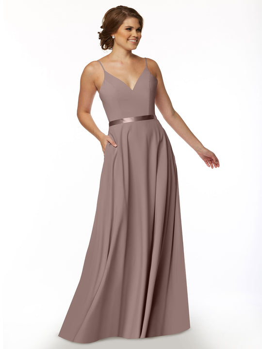 A woman wearing Avery Austin’s 80112— a sleeveless, floor-length mauve A-line dress with V-neckline and satin waistband— stands smiling against a plain white background.