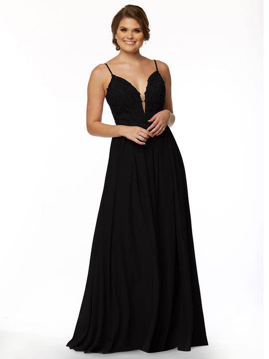 A woman stands smiling against a white background wearing the Avery Austin 80113, a sleeveless black evening gown with an illusion plunge neckline and lace bodice.