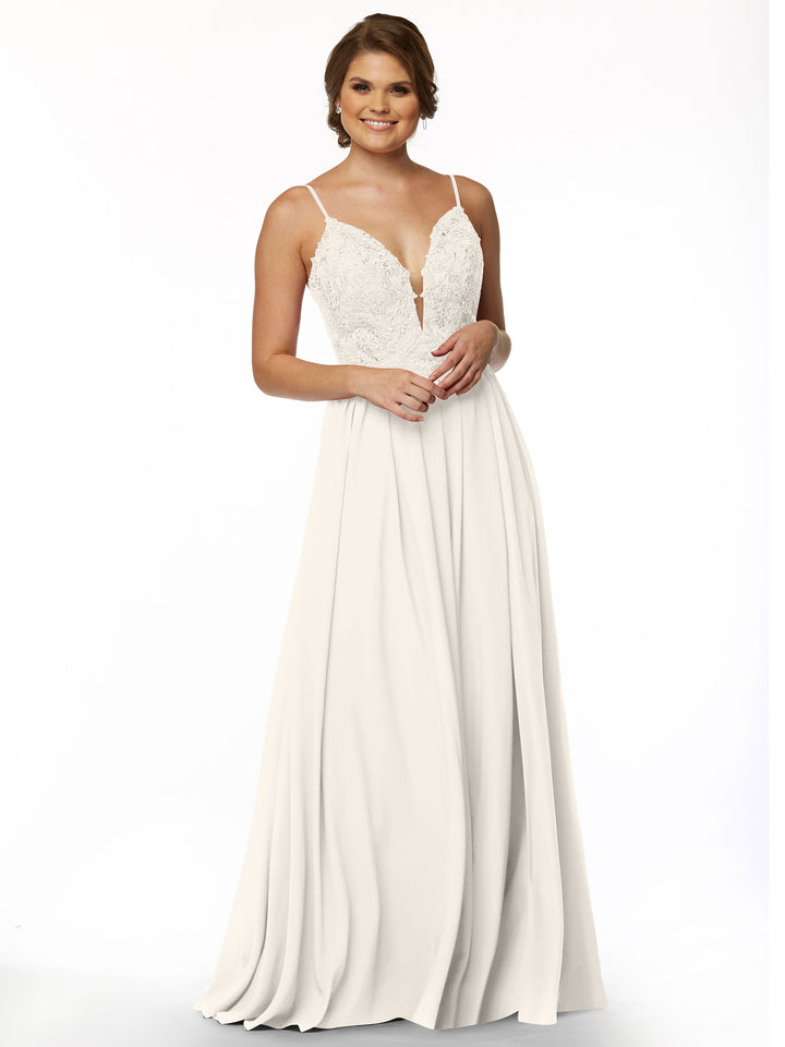 A woman smiles with her hands clasped, modeling Avery Austin’s 80113—a sleeveless white gown with a lace bodice, illusion plunge neckline, thin straps, and an A-Line chiffon skirt—against a plain white background.
