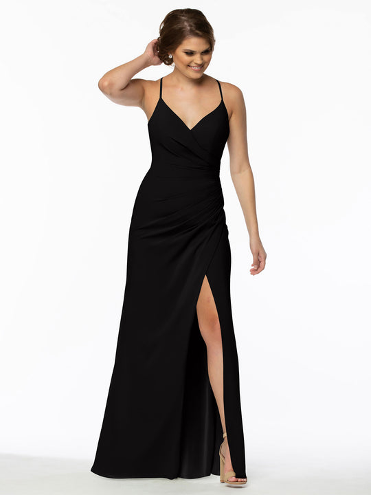 A woman in Avery Austin’s 80114 dress—sleeveless, floor-length, V-neck with a thigh-high slit—stands smiling with one hand touching her hair against a plain white backdrop.