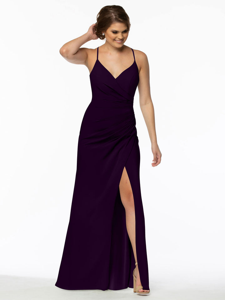A woman models Avery Austin style 80114, a sleeveless, floor-length deep purple v-neck bridesmaid dress with spaghetti straps and a high slit, standing against a white background, smiling as she touches her hair.