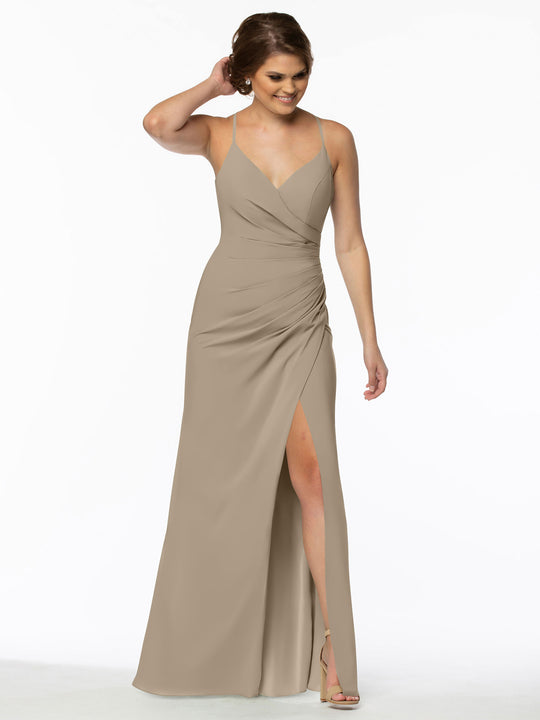 A woman models the Avery Austin 80114: a sleeveless taupe chiffon bridesmaid dress with V-neck, ruched waist, and high slit. She smiles against a white background, wearing strappy heels and touching her hair.